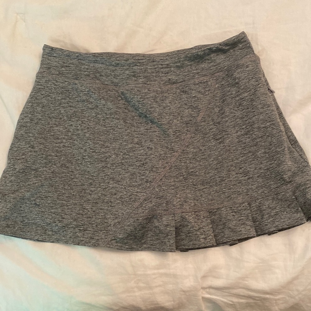 Gray tennis skirt with left zip pocket. Ruffle on left leg.